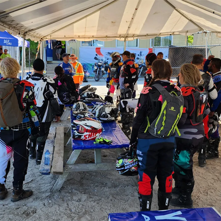 Group of riders gathered under a tent with helmets and gear on tables.