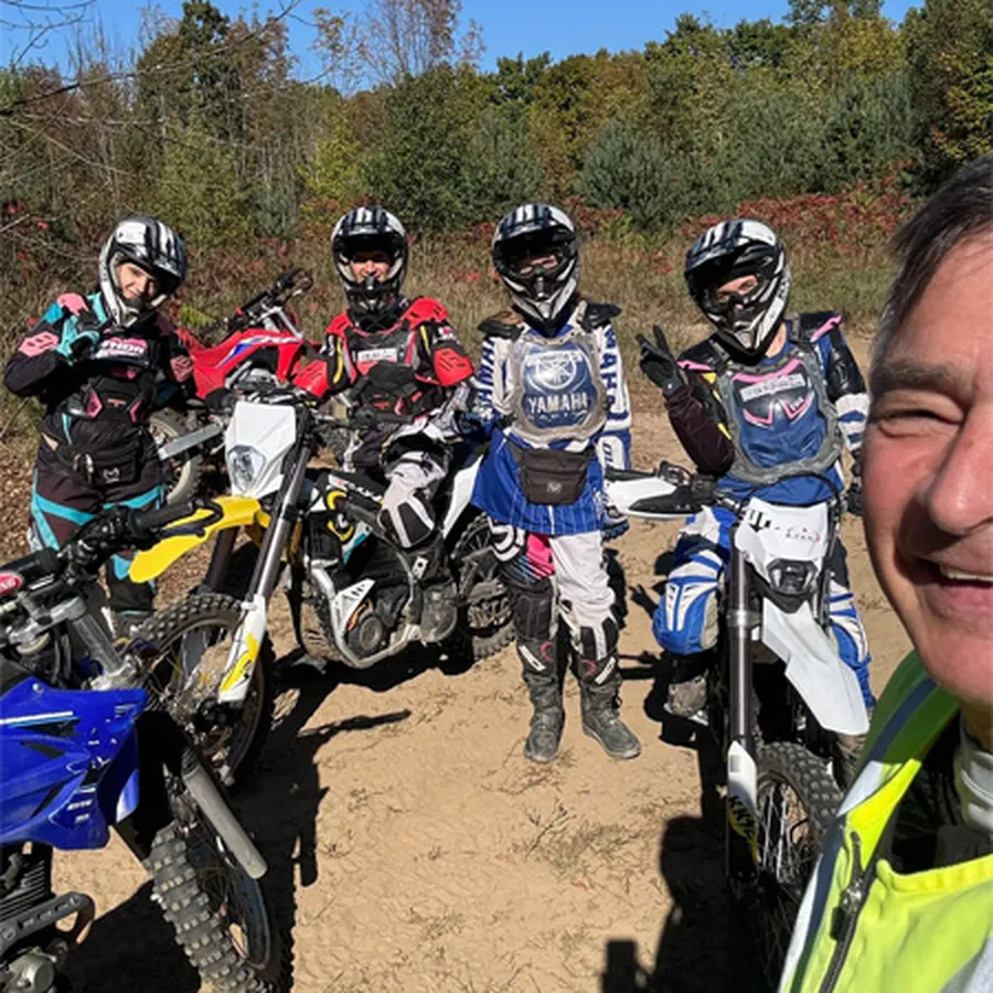 Group of dirt bike riders standing with their bikes on a dirt trail.