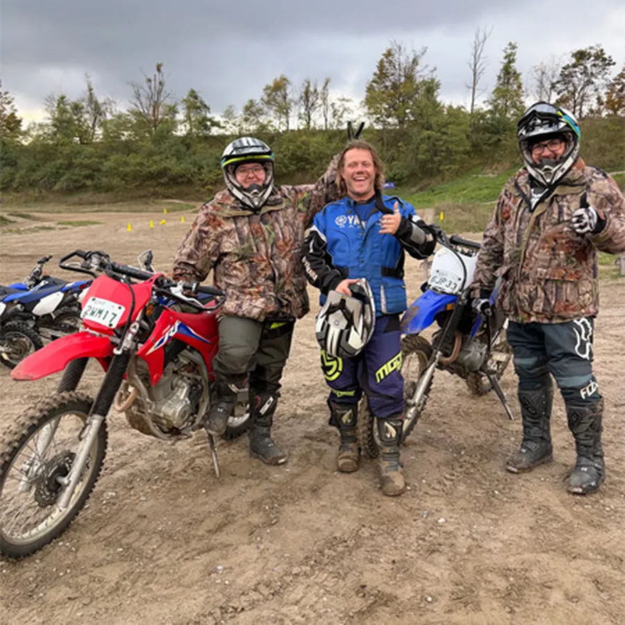Three dirt bike riders standing with their bikes on a muddy track.
