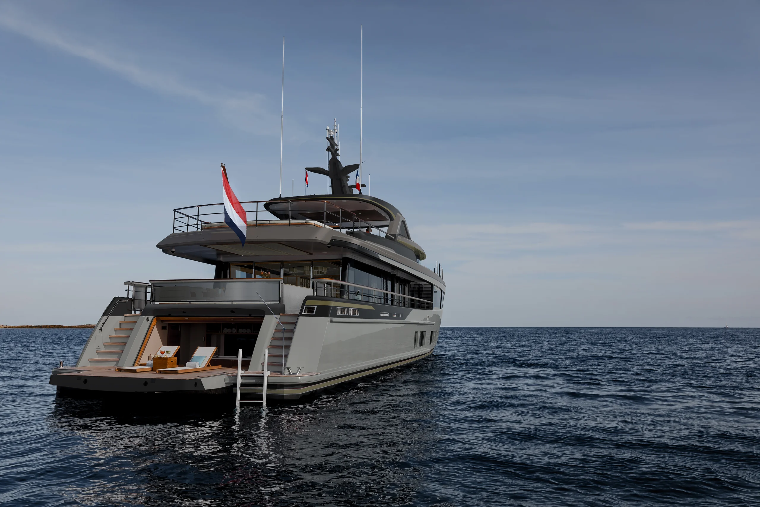 A luxury Mulder BN143 yacht anchored on calm waters under a clear sky, with a Dutch flag flying at the stern and an open deck area with seating.