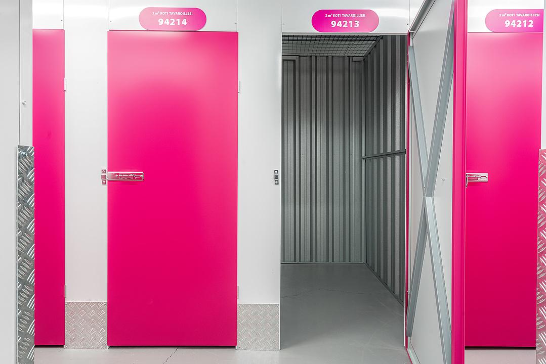 Pink doors to storage units, one open revealing a metal-walled interior. Number plates are above each door.