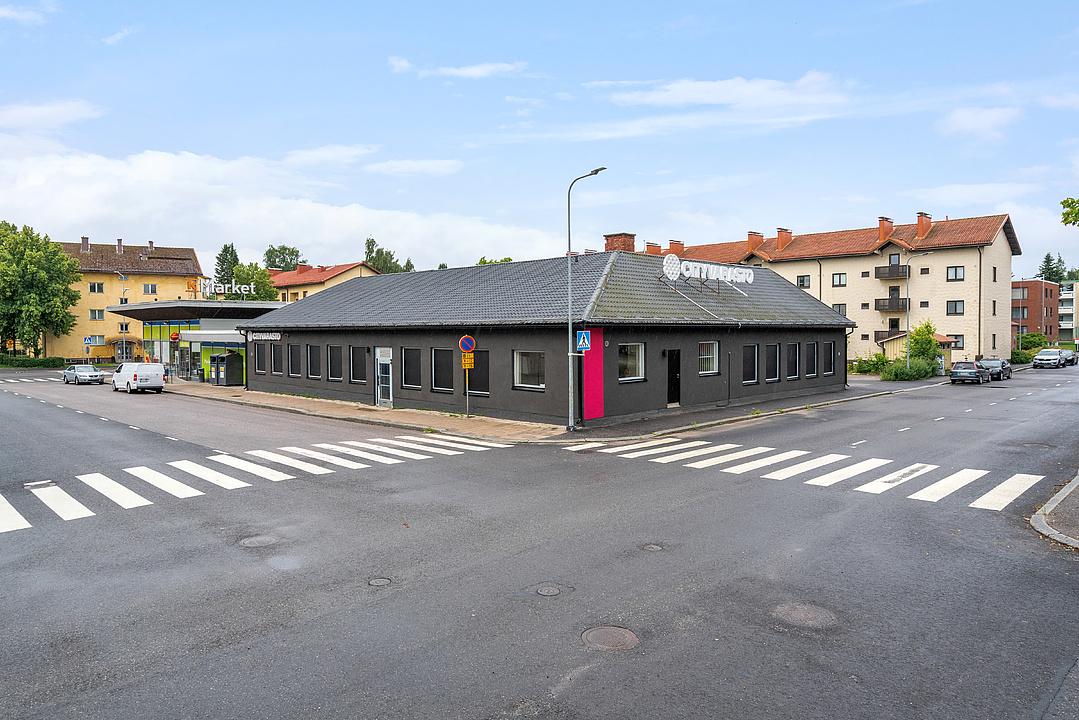 Single-story gray building on a street corner with multiple pedestrian crossings and residential apartments in the background.