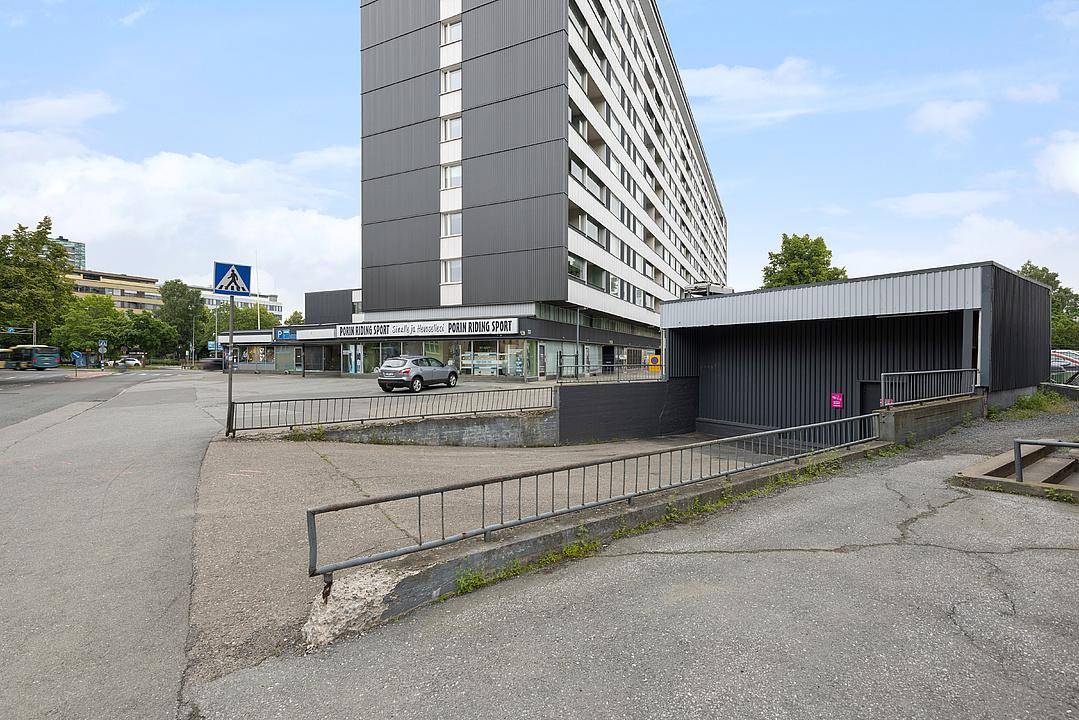 A tall, gray building with a "Porin Riding Sport" store at the base, a parked car, and a concrete ramp leading to a covered area.