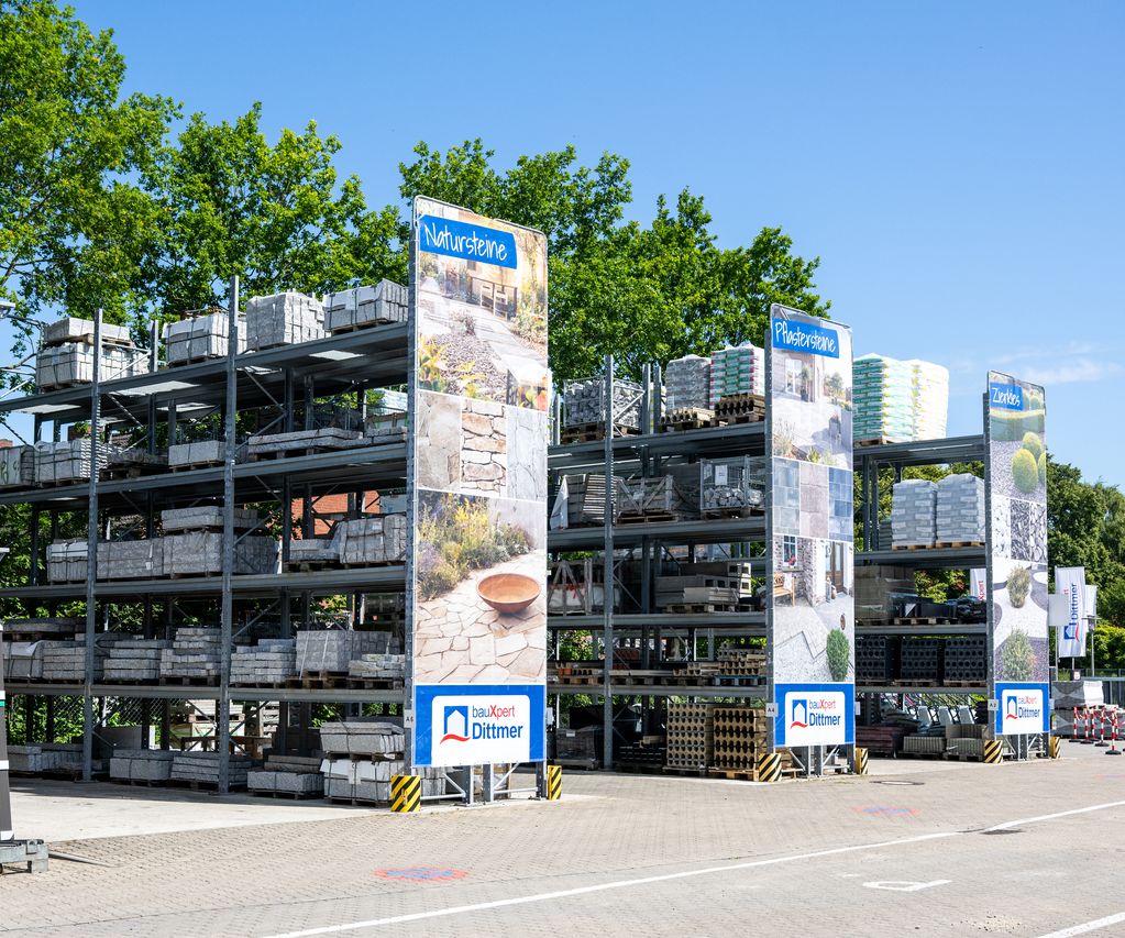 Lagerregale mit Palettenware im Außenbereich von bauXpert Dittmer, mit Schildern für Natursteine und Pflastersteine