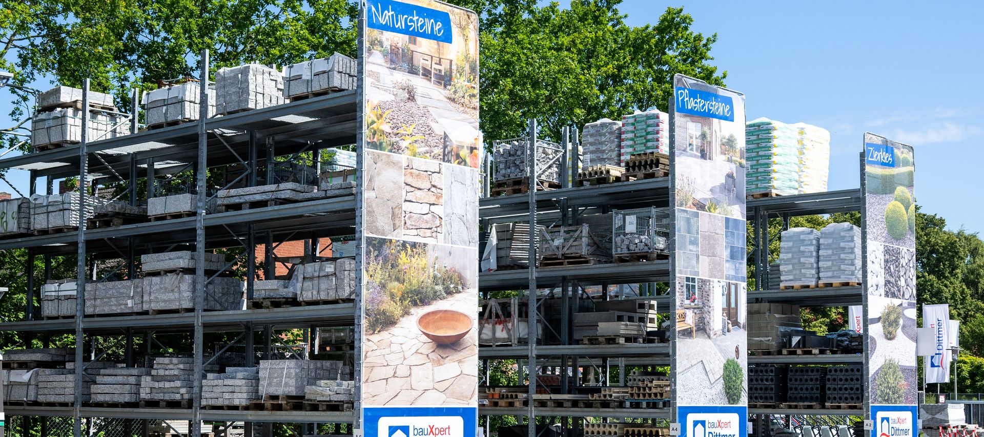 Lagerregale mit Palettenware im Außenbereich von bauXpert Dittmer, mit Schildern für Natursteine und Pflastersteine