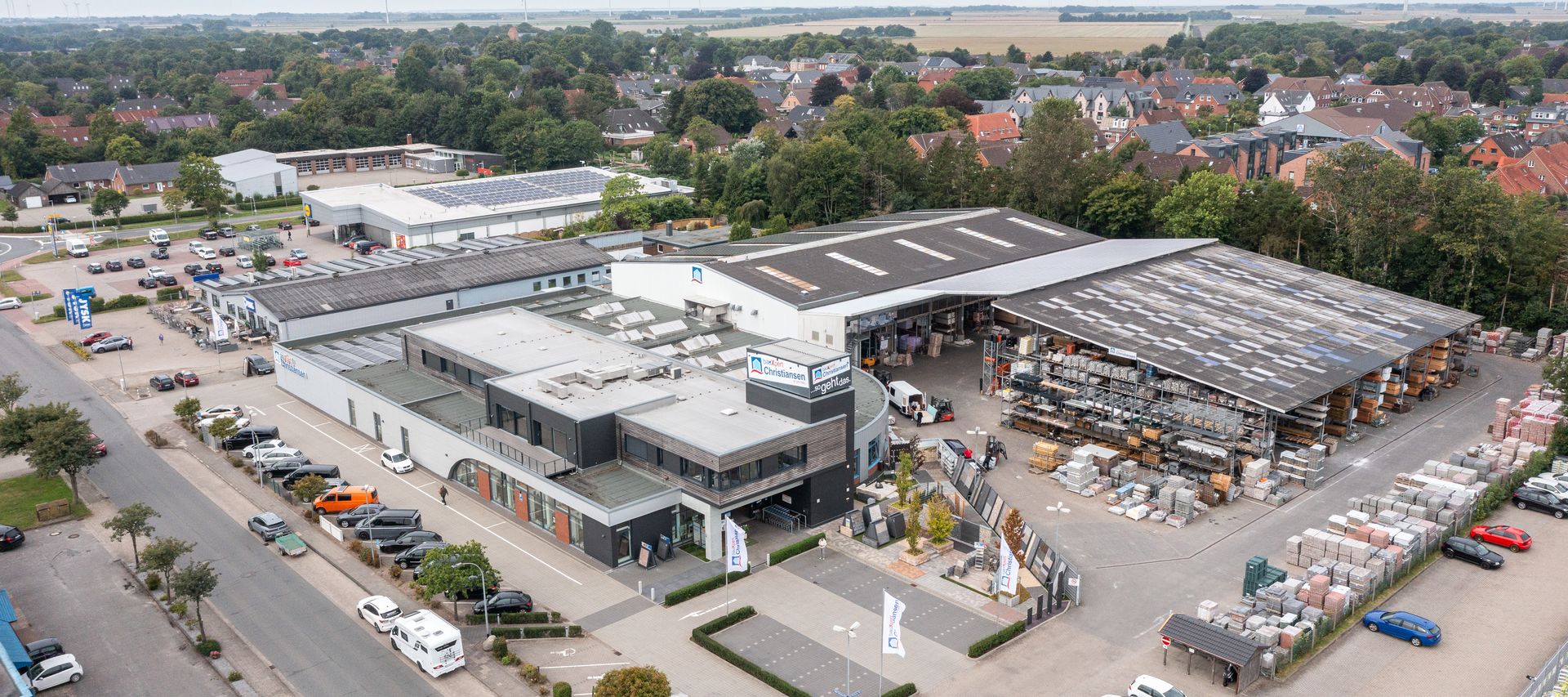 Luftaufnahme vom bauXpert Christiansen Standort mit Fachmarkt, Lagerhallen, Außenlager und Parkplatz