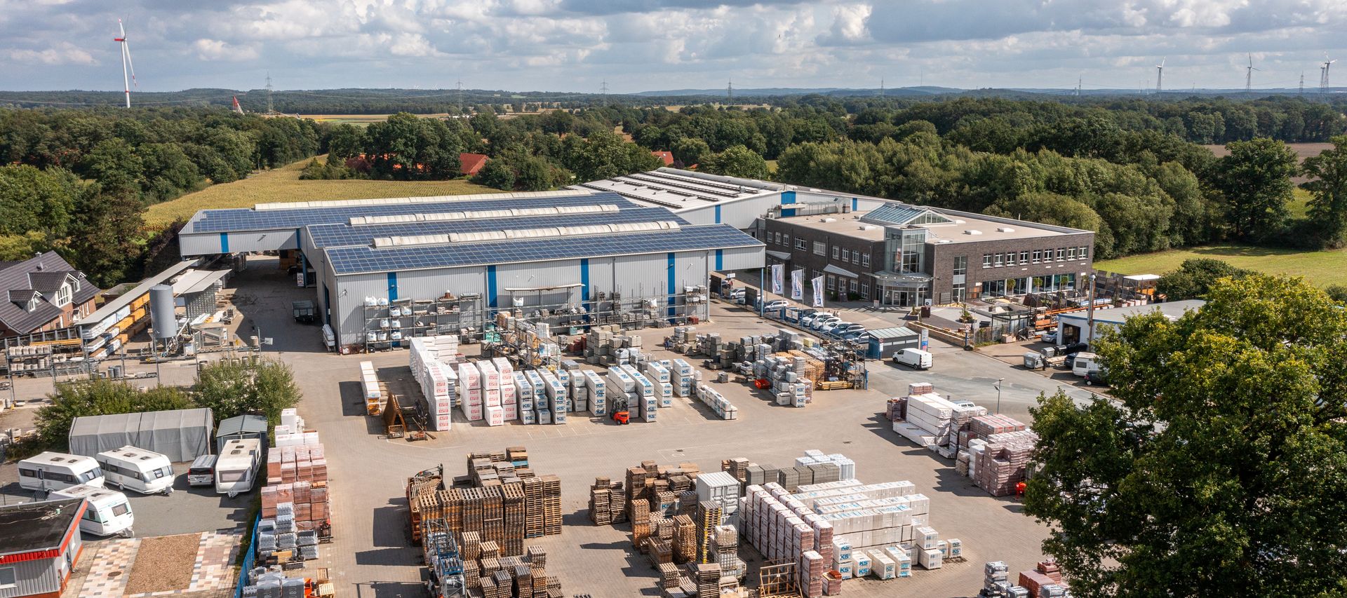 Luftaufnahme vom bauXpert Standort mit Lagerhallen, Außenlager und Baustoff-Paletten auf dem Hof