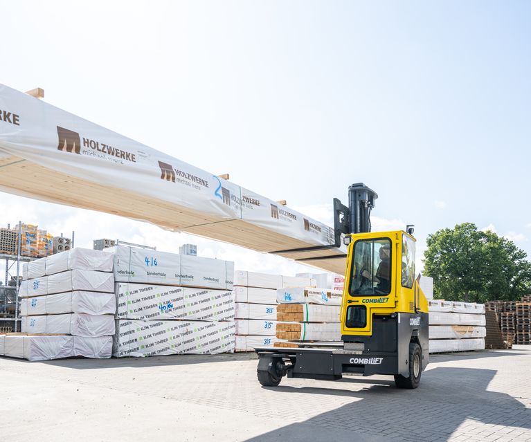 Seitenstapler transportiert lange Holzpakete im Außenlager von bauXpert Seelmeyer
