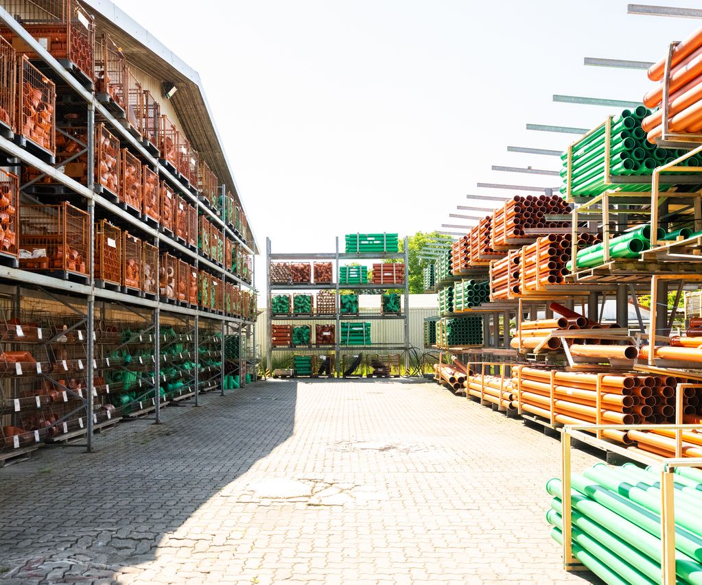 Lagerplatz mit Regalen voller orangefarbener und grüner KG-Rohre und Formteile