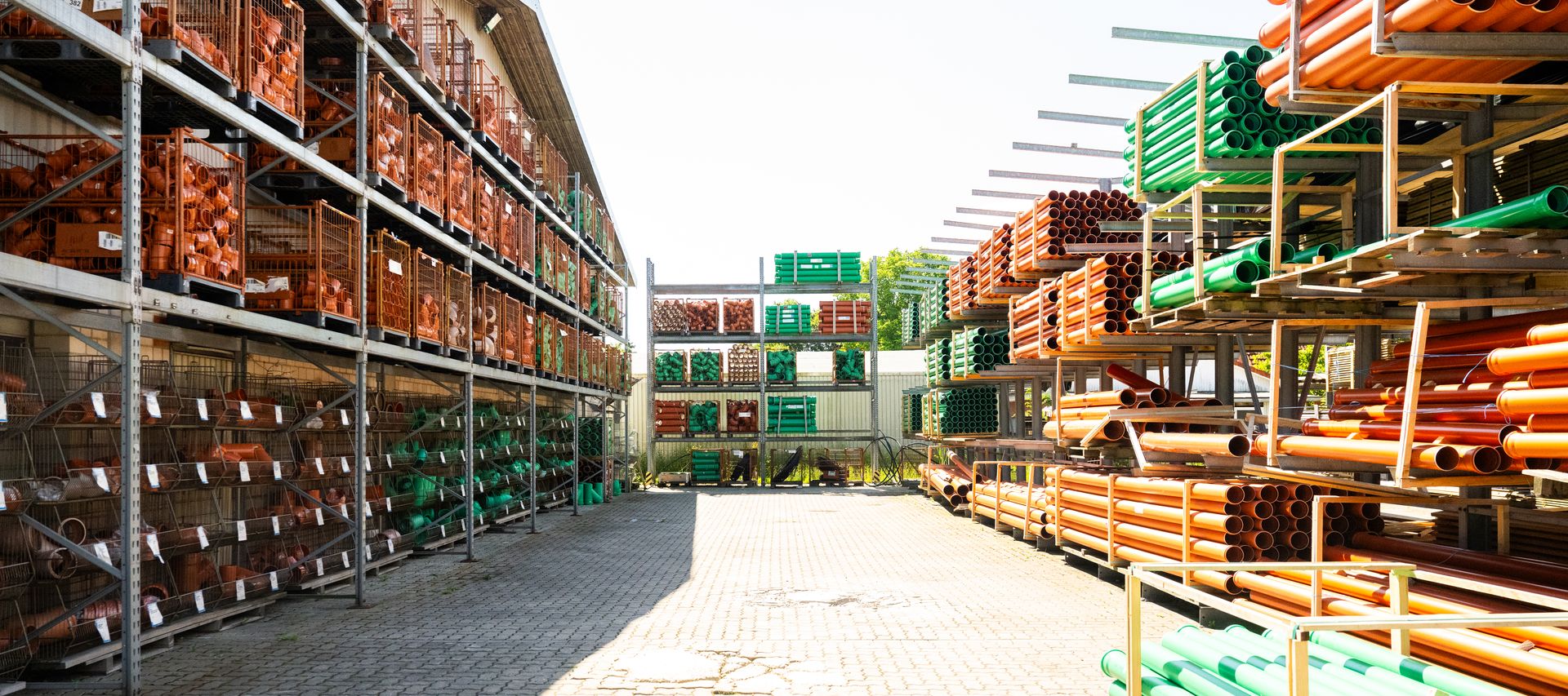 Lagerplatz mit Regalen voller orangefarbener und grüner KG-Rohre und Formteile