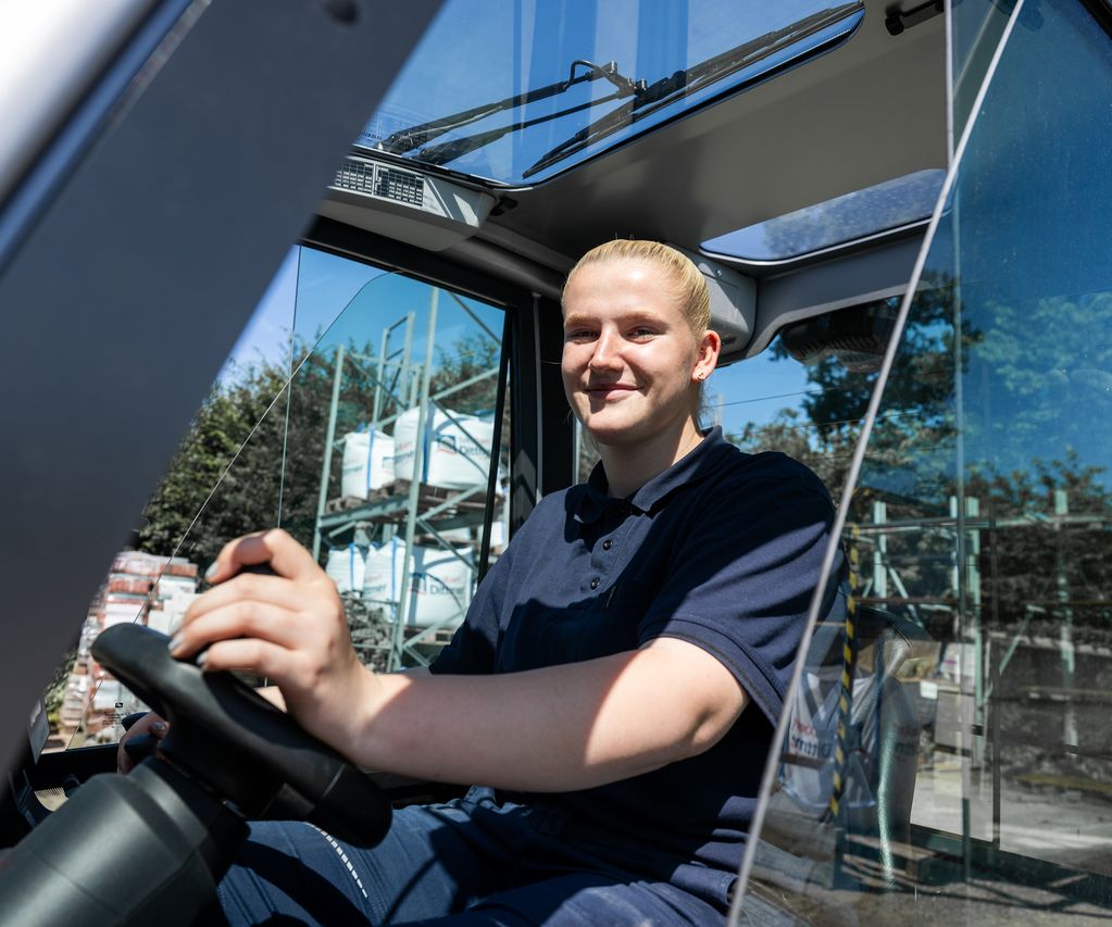 Auszubildende bei bauXpert Dittmer sitzt am Steuer eines Gabelstaplers auf dem Betriebshof und arbeitet in der Lagerlogistik.