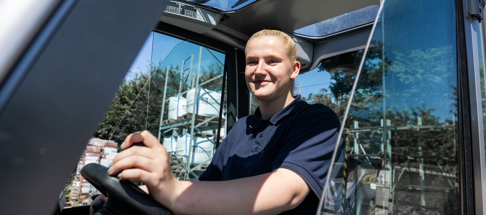 Auszubildende bei bauXpert Dittmer sitzt am Steuer eines Gabelstaplers auf dem Betriebshof und arbeitet in der Lagerlogistik.