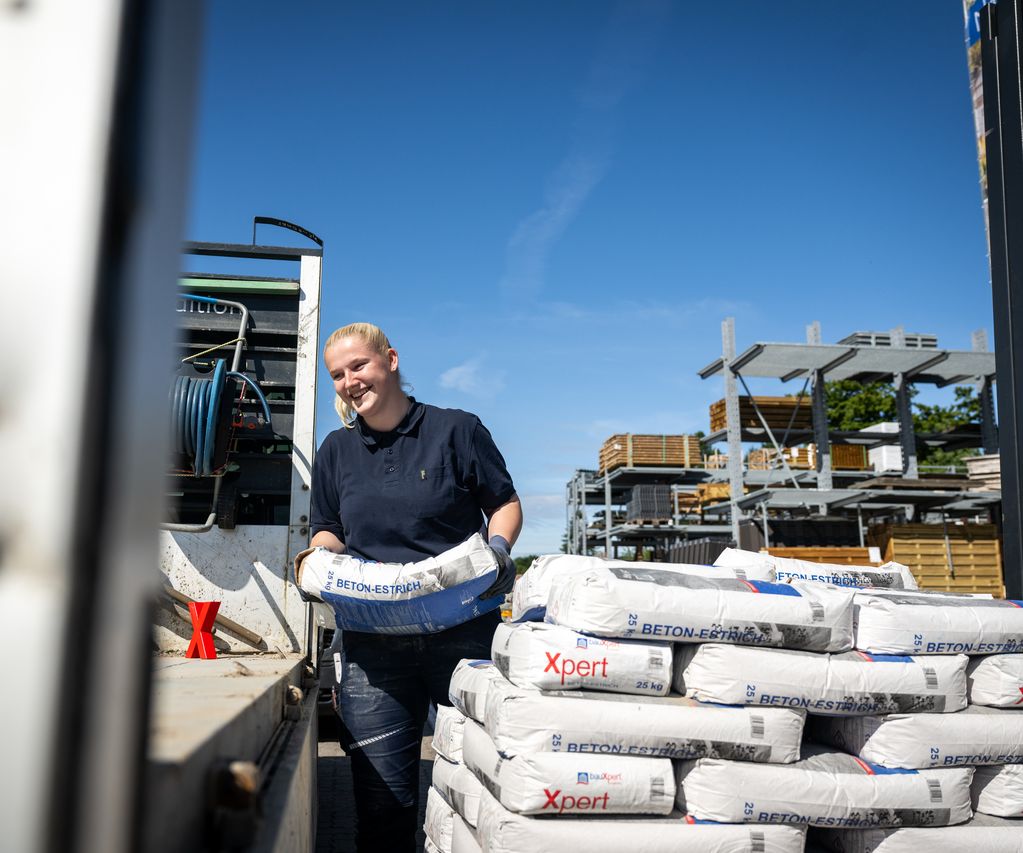 Mitarbeiterin verladen Xpert Beton-Estrich Säcke auf Lkw im Baustoffhandel