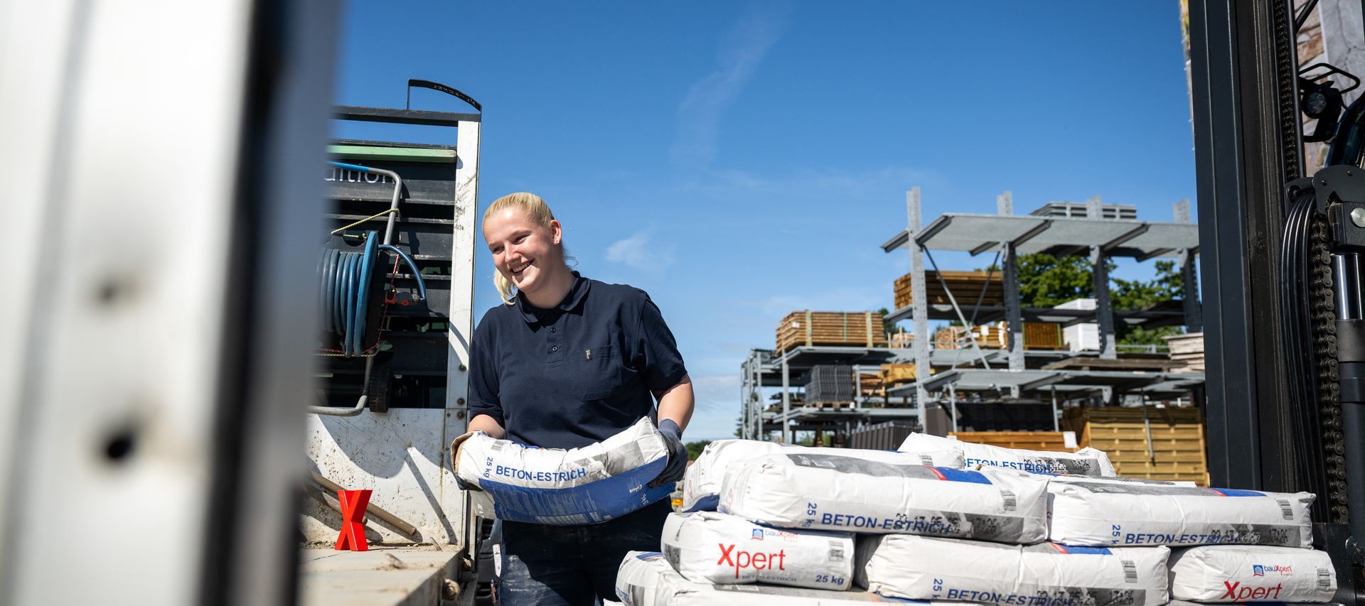 Mitarbeiterin verladen Xpert Beton-Estrich Säcke auf Lkw im Baustoffhandel