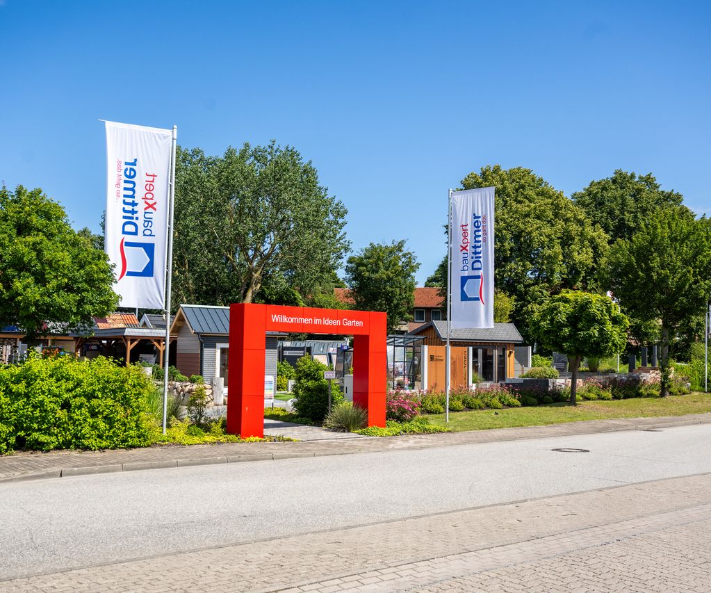 Eingang zur Gartenausstellung bei bauXpert Dittmer mit rotem Torbogen und Fahnen an der Straße