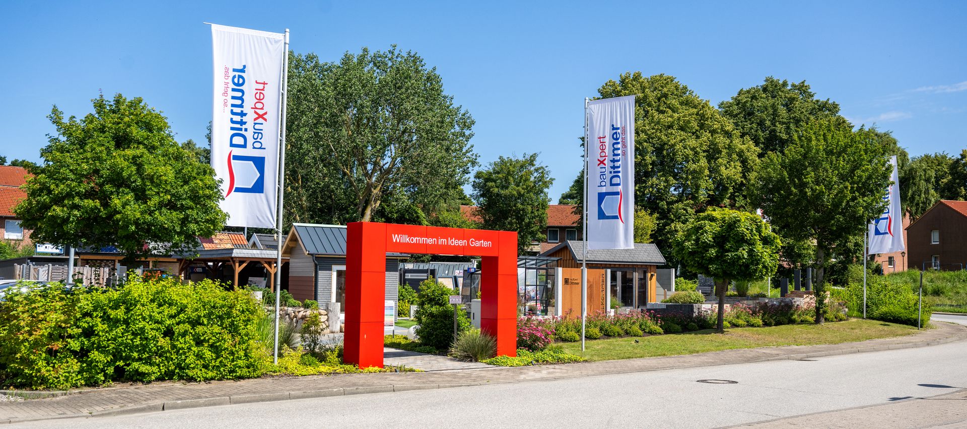 Eingang zur Gartenausstellung bei bauXpert Dittmer mit rotem Torbogen und Fahnen an der Straße
