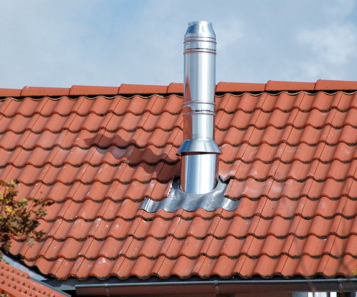 Edelstahlschornstein ragt durch ein geneigtes Ziegeldach eines Wohnhauses, sauber eingefasst und wetterfest montiert.