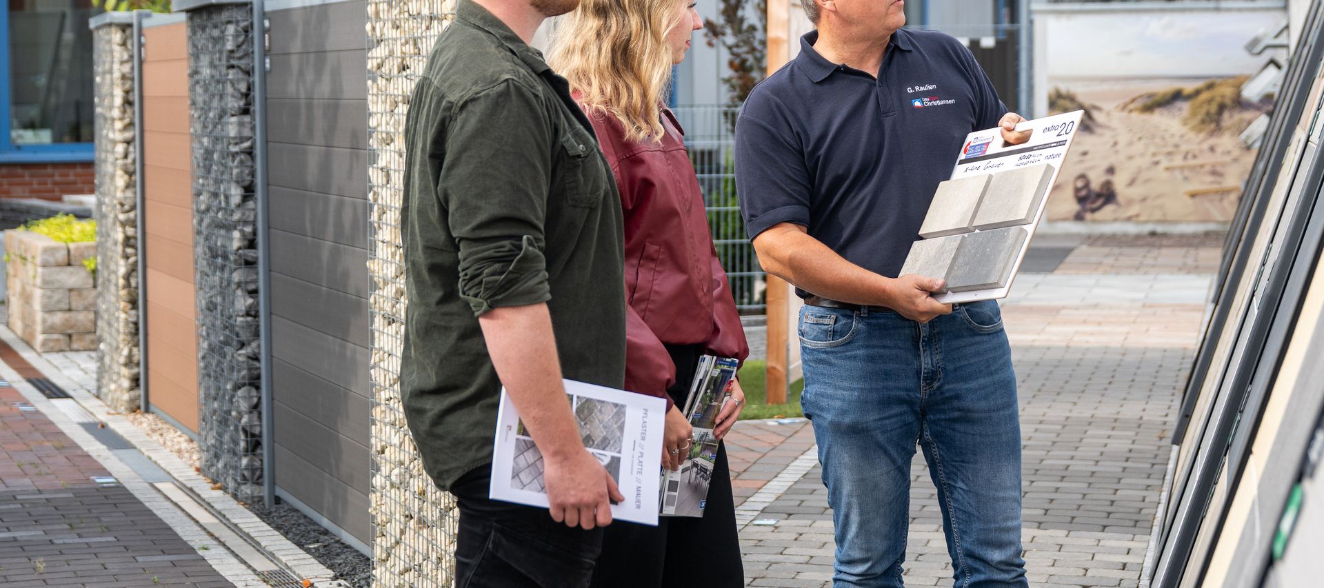 Kunde und Fachberater stehen vor Musterflächen und besprechen die Gestaltung einer Terrasse.