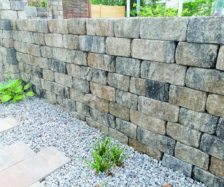 Eine Trockenmauer aus Natursteinen stützt einen Hang und fügt sich harmonisch in die Gartenlandschaft ein.