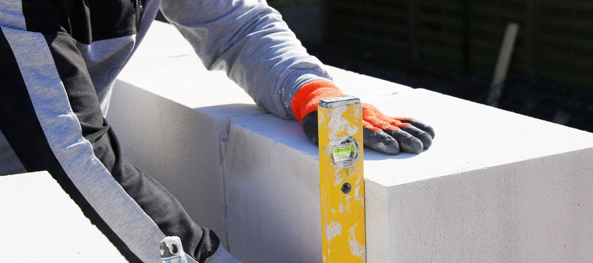 Ein Arbeiter hält eine Wasserwaage an eine Kalksandsteinwand, um die exakte Ausrichtung des Mauerwerks zu prüfen.