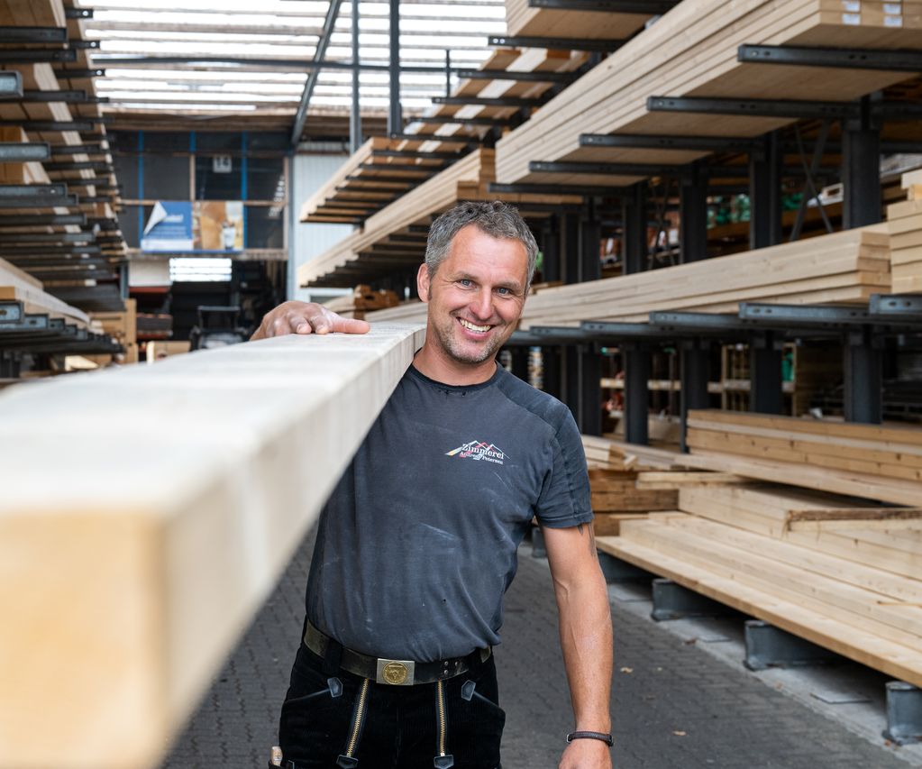 Ein Mitarbeiter trägt Holzbalken durch die Lagerhalle und bereitet sie für die Ausgabe vor.