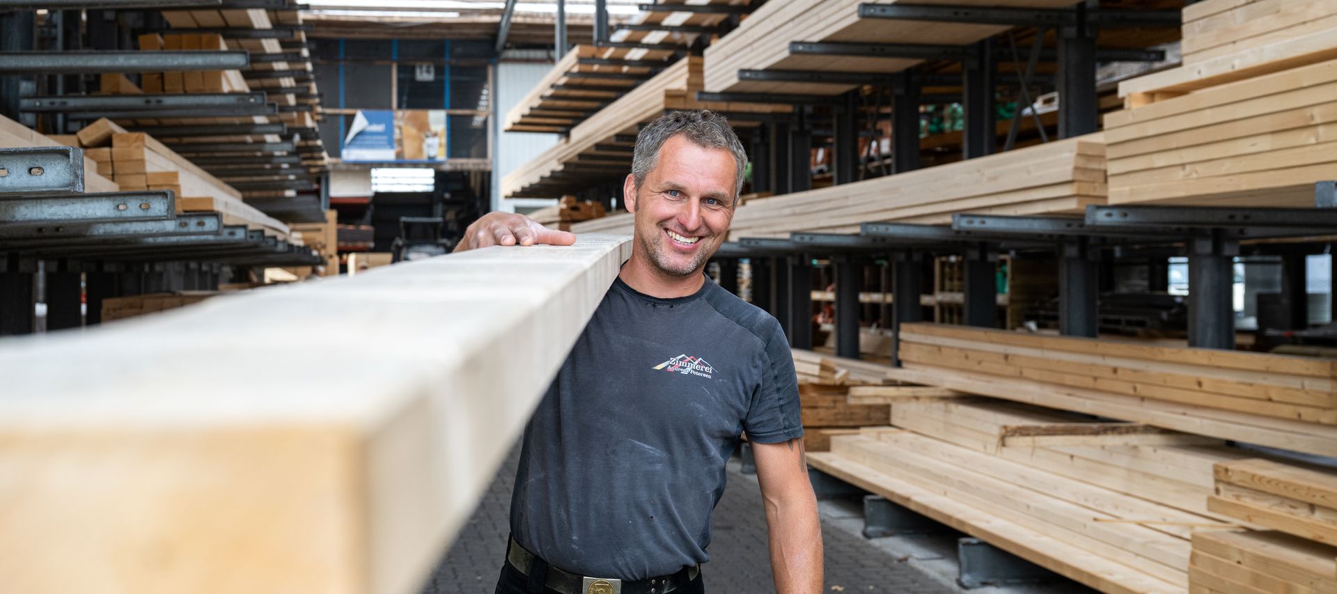 Ein Mitarbeiter trägt Holzbalken durch die Lagerhalle und bereitet sie für die Ausgabe vor.