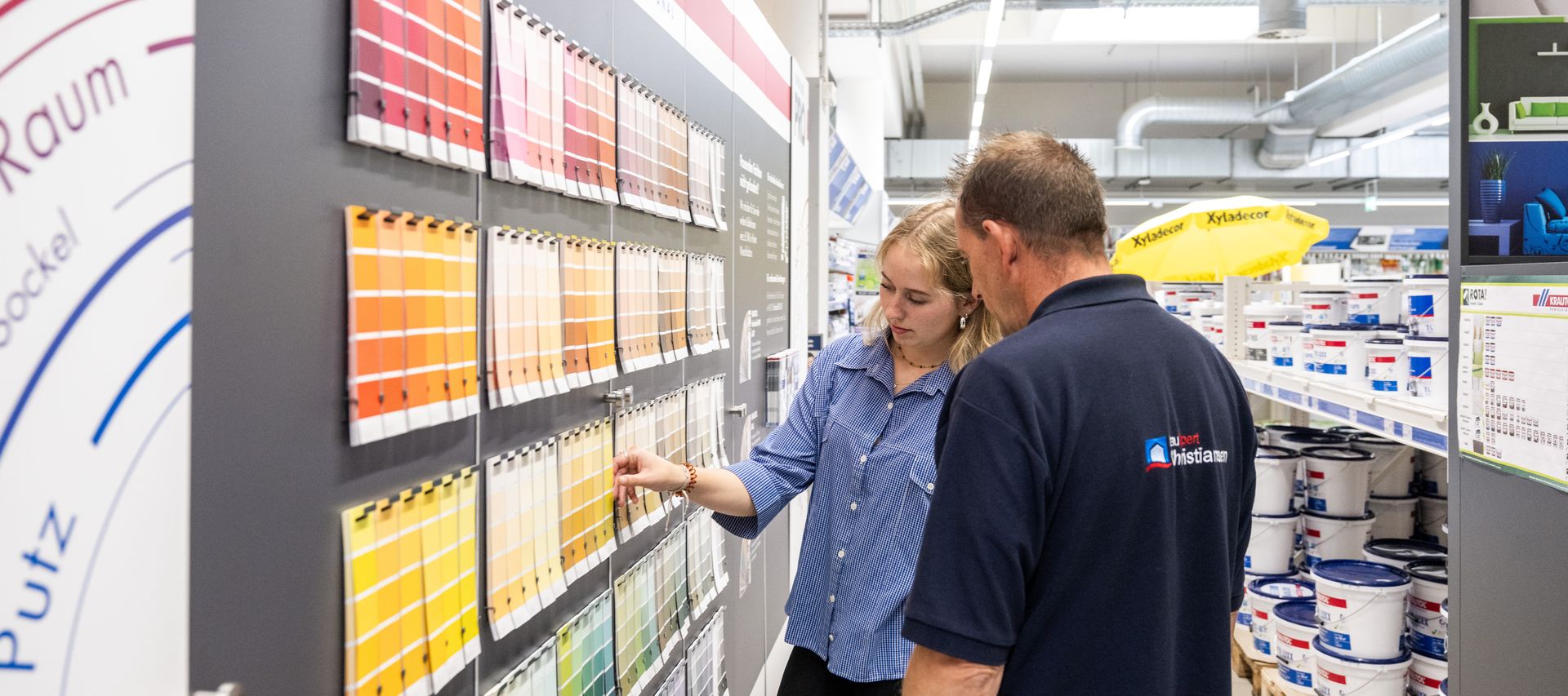 Eine Kundin vergleicht unterschiedliche Wandfarben und erhält Unterstützung bei der Produktauswahl.