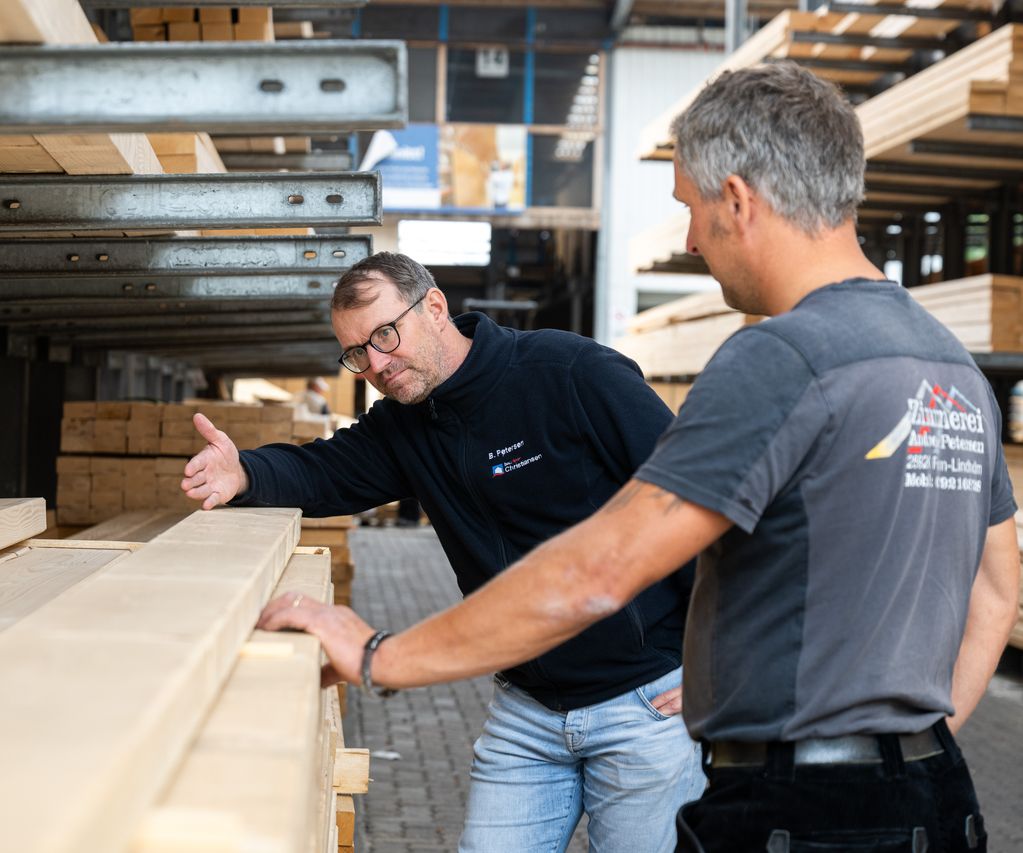 Ein Mitarbeiter berät Geschäftskunden aus einer Zimmerei zu passenden Materialien im Lagerbereich.