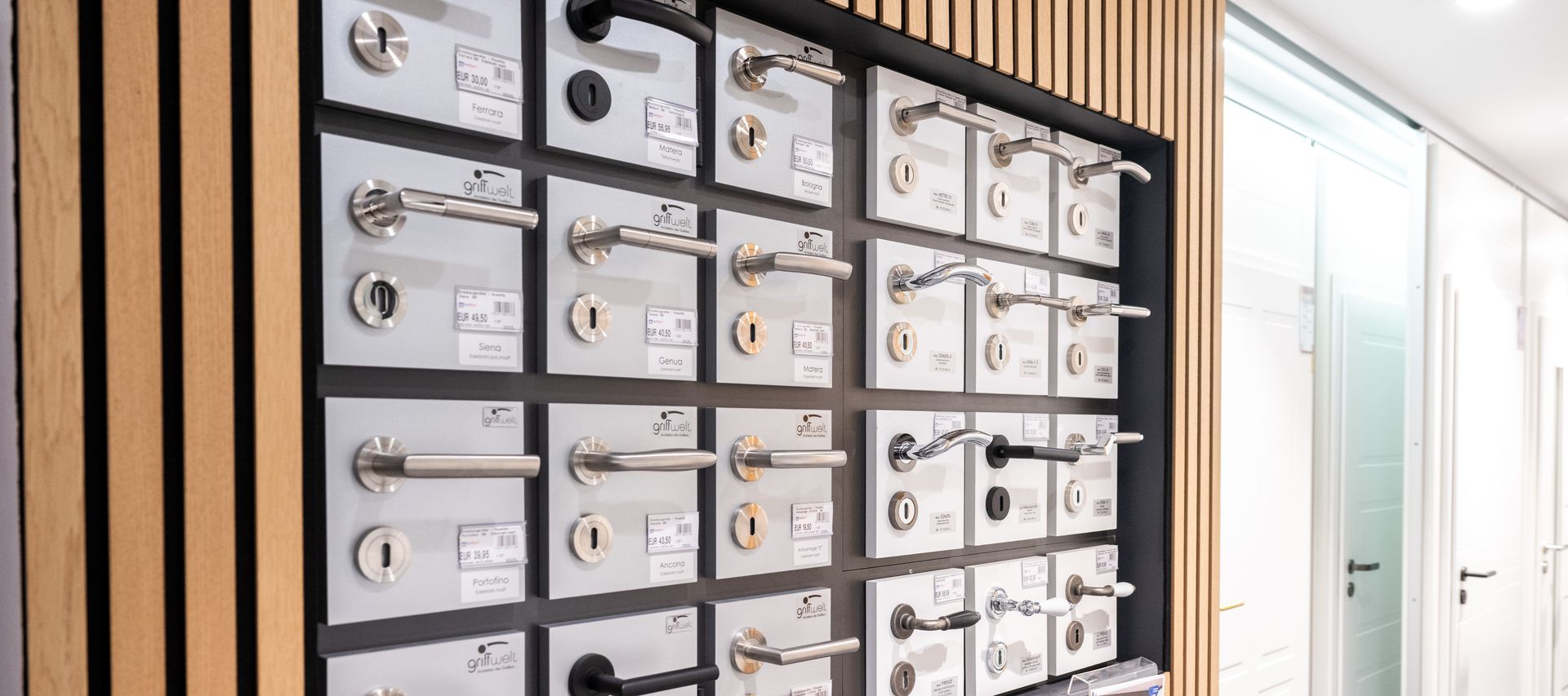 Verschiedene Türklinken und Beschläge sind übersichtlich auf einer Präsentationswand angeordnet.