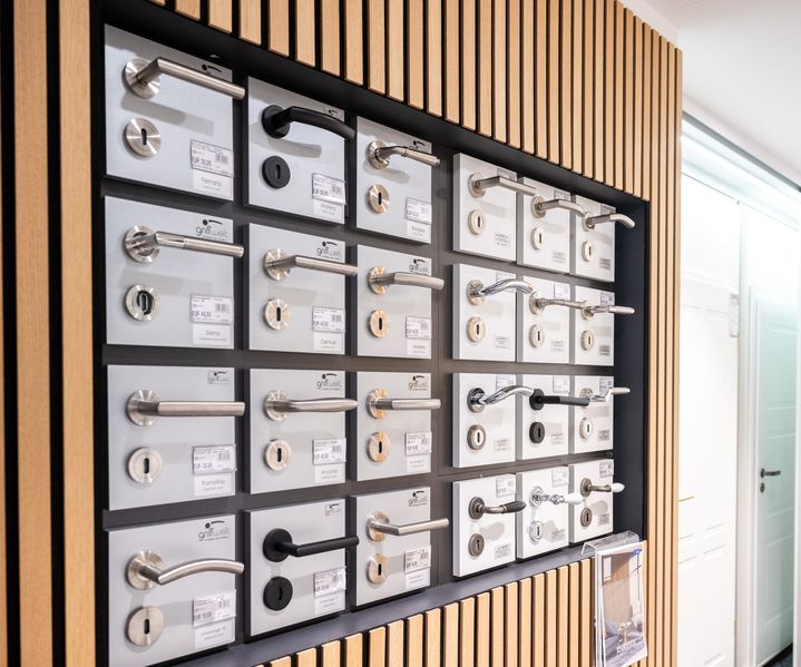 Verschiedene Türklinken und Beschläge sind übersichtlich auf einer Präsentationswand angeordnet.