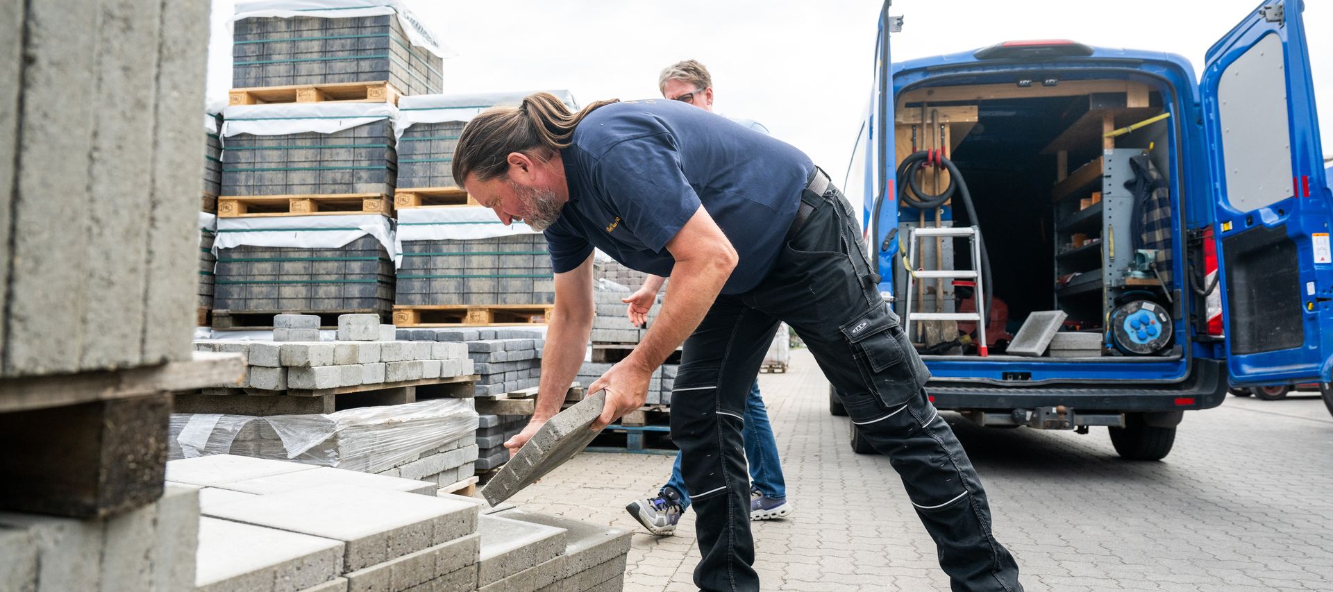 Ein Mitarbeiter erklärt einem Kunden die Eigenschaften von Pflastersteinen für den Außenbereich.