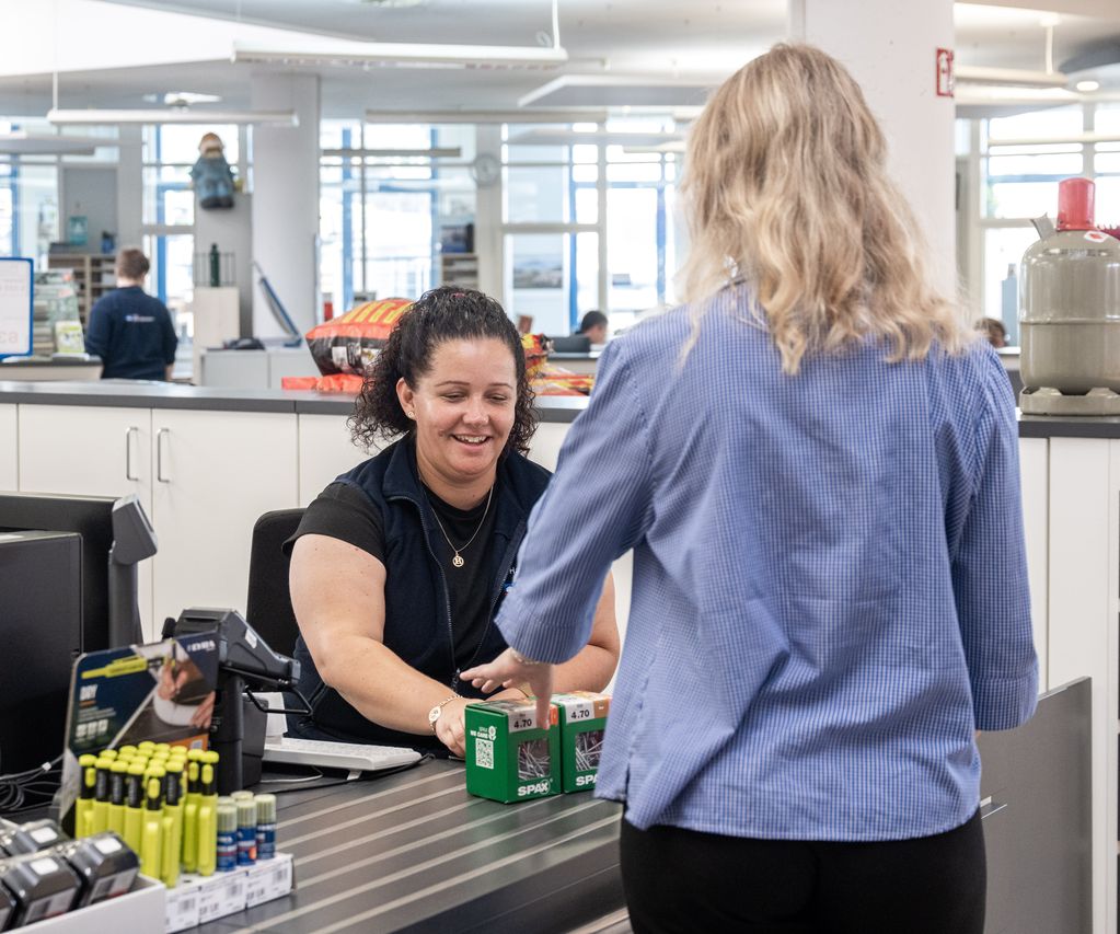 Eine Kundin steht vor einem Regal mit Schrauben und wählt die passende Packung für ihr Projekt aus.