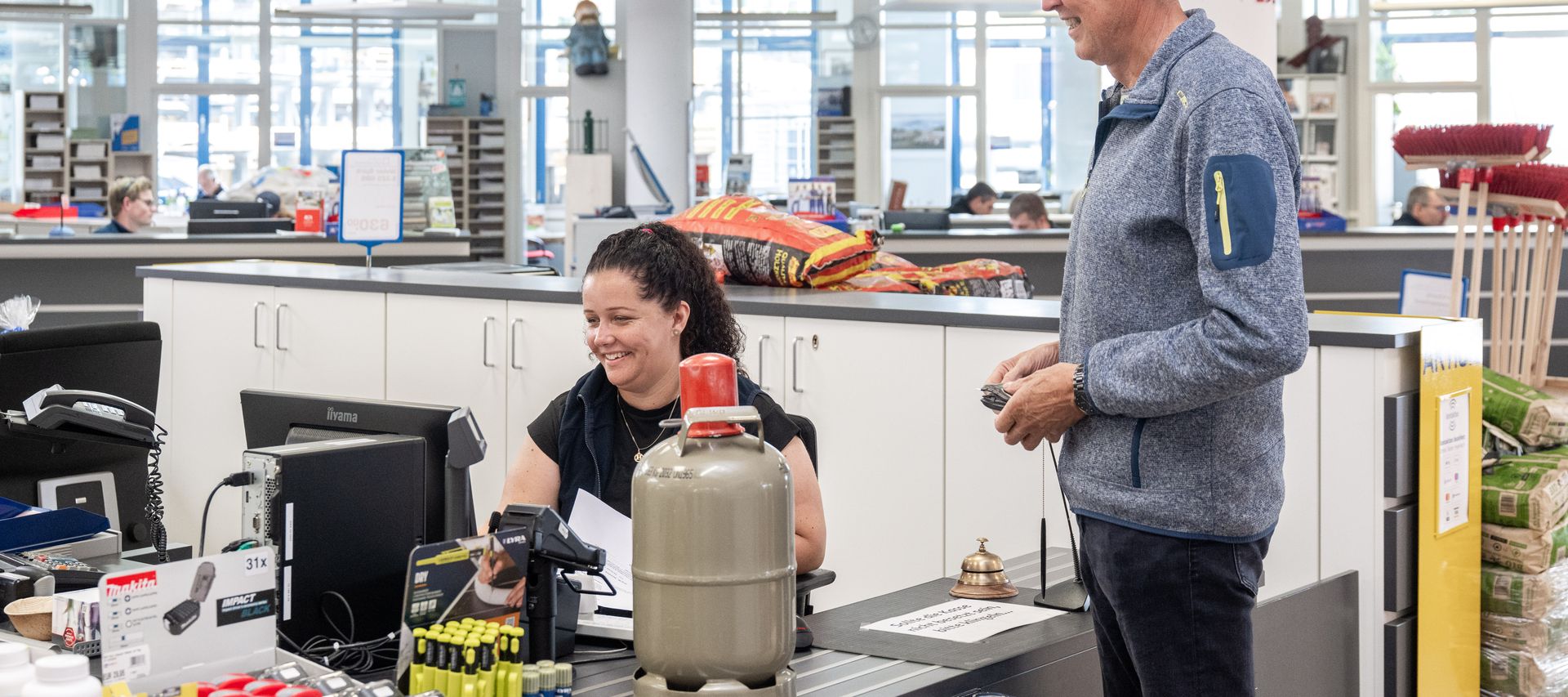 Kunde erhält eine Gasflasche vom Mitarbeiter an der Verkaufsstelle im Fachhandel.