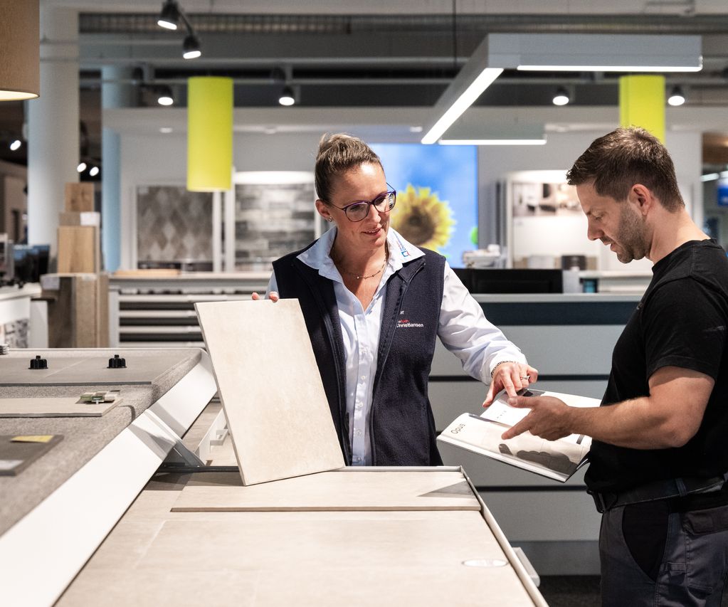 Fachberaterin zeigt Kunden verschiedene Fliesenmuster in einem Showroom für Innenraumgestaltung.