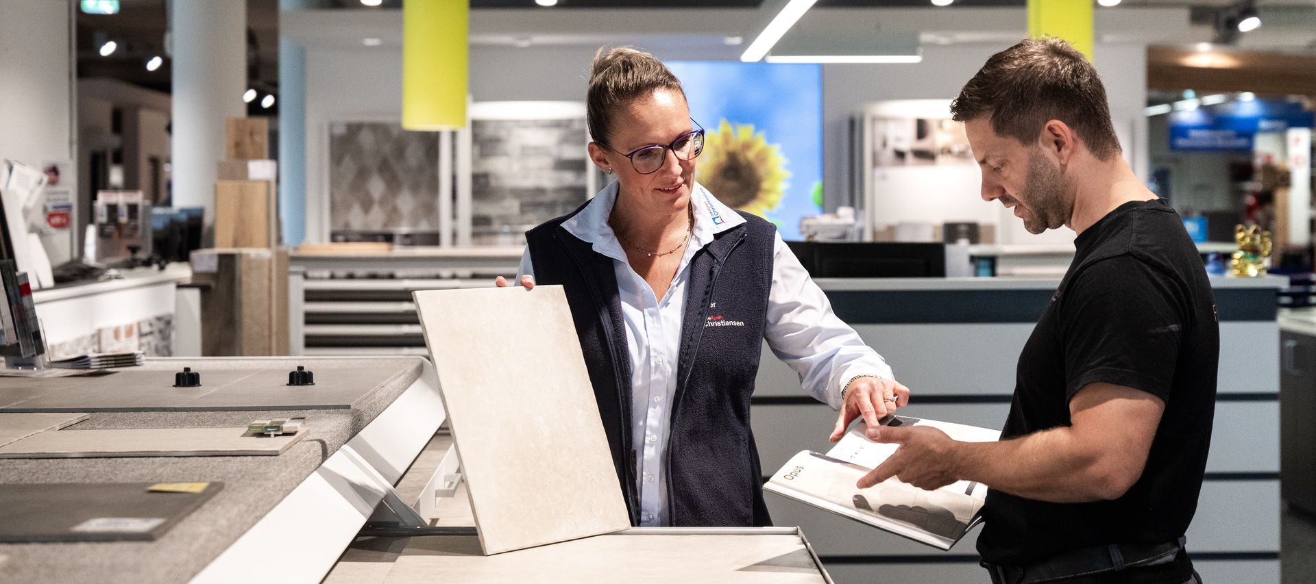 Fachberaterin zeigt Kunden verschiedene Fliesenmuster in einem Showroom für Innenraumgestaltung.
