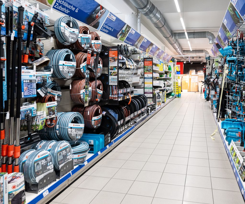 Gartenschläuche und Gartenartikel hängen säuberlich sortiert in einem Baumarkt Gang