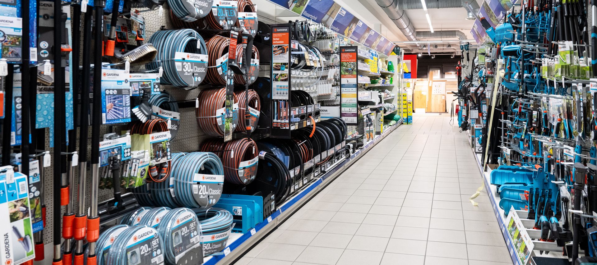 Gartenschläuche und Gartenartikel hängen säuberlich sortiert in einem Baumarkt Gang