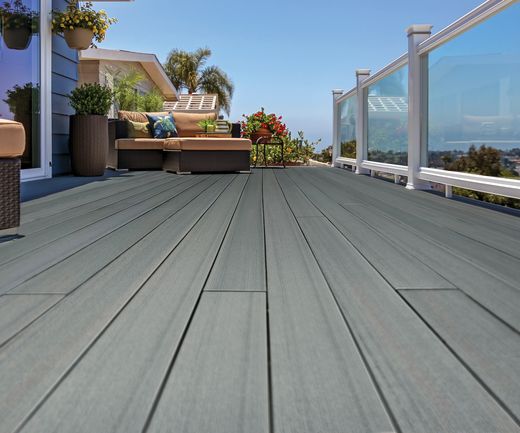 Großzügige Terrasse mit grau nuancierten WPC-Dielen, Sitzlounge, Glasgeländer und Blick ins Grüne.
