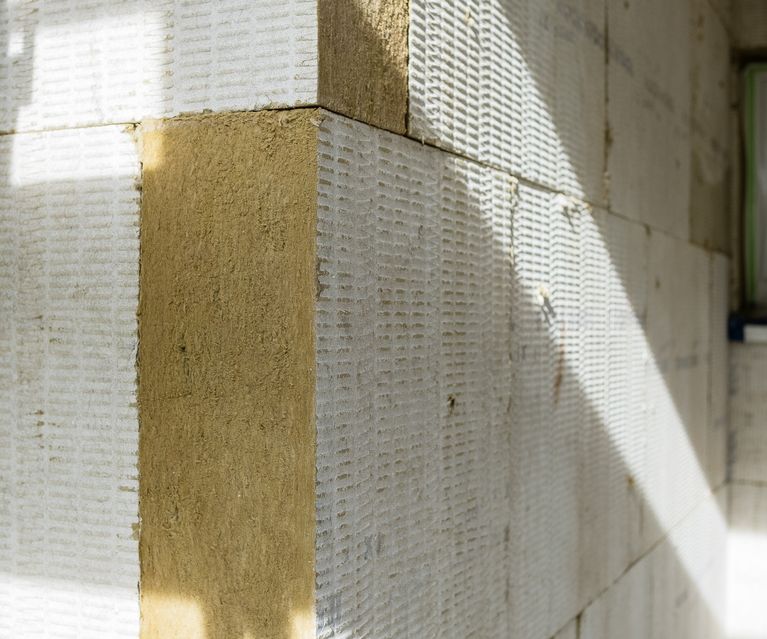 Detailaufnahme einer gedämmten Gebäudewand mit weißen Dämmplatten und beigem Eckschutz, im Sonnenlicht