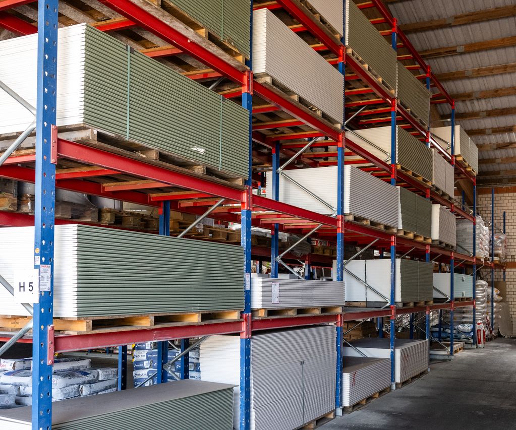 Lagerregale mit gestapelten Gipskartonplatten auf Paletten bei bauXpert Dittmer in Lütjenburg, sortiert nach Farbe und Typ