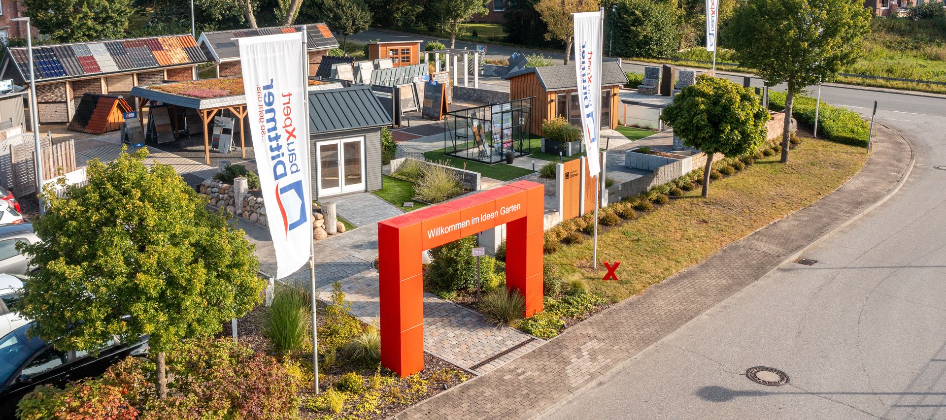 Luftaufnahme des Ideen-Gartens bei bauXpert Dittmer mit Musterhäusern, Ausstellungsflächen und Eingangstor mit rotem Bogen