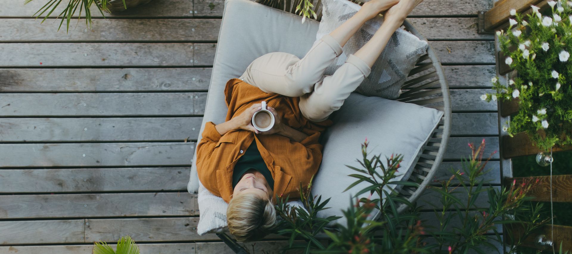 Person entspannt mit einer Tasse Kaffee in einem Loungesessel auf einer Holzterrasse