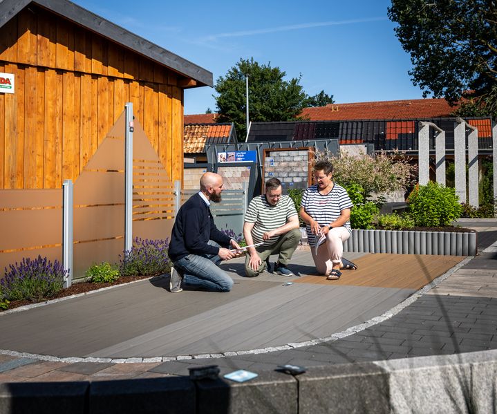 Mitarbeiter berät zwei Kunden zu Terrassendielen und Sichtschutz in der Gartenausstellung von bauXpert Dittmer in Lütjenburg