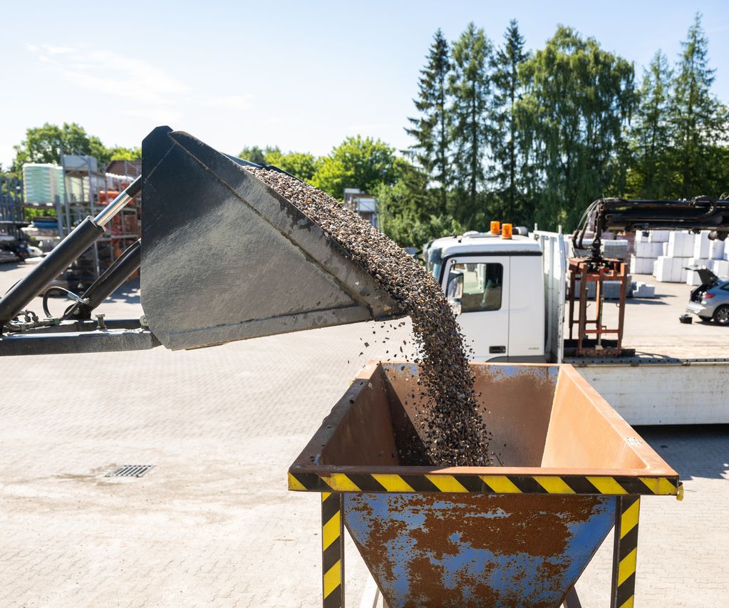 Ein Radlader füllt Kies in einen Metalltrichter, darunter steht ein Big Bag mit dem Logo von bauXpert Dittmer in Lütjenburg.