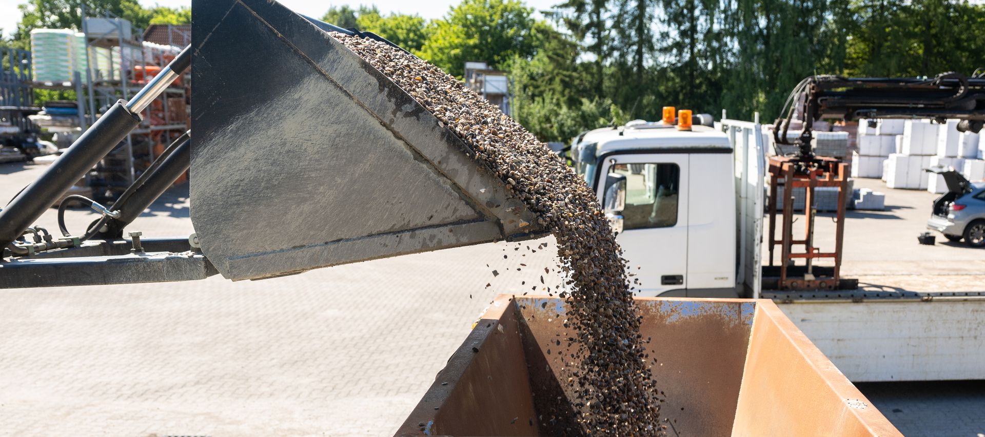 Ein Radlader füllt Kies in einen Metalltrichter, darunter steht ein Big Bag mit dem Logo von bauXpert Dittmer in Lütjenburg.