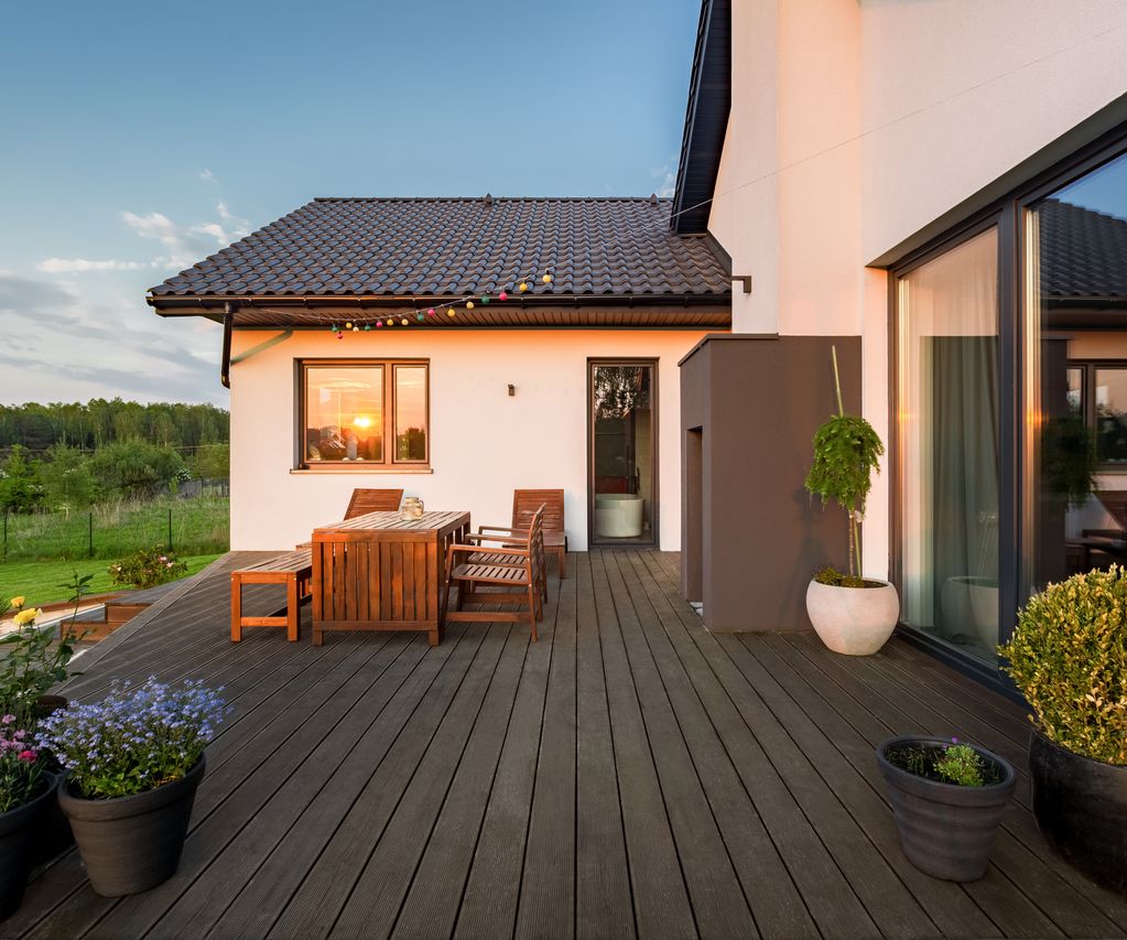 Dunkle Terrassendielen mit Sitzgruppe und Pflanzkübeln an einem Einfamilienhaus bei Abendlicht