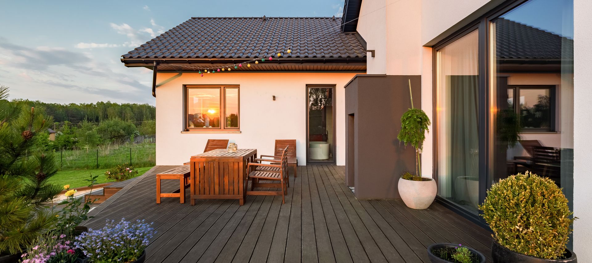 Dunkle Terrassendielen mit Sitzgruppe und Pflanzkübeln an einem Einfamilienhaus bei Abendlicht