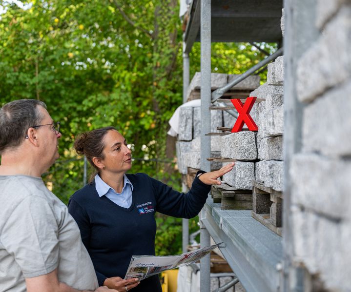 Persönliche Beratung bei bauXpert Dittmer im Außenlager: Mitarbeiterin zeigt Pflastersteine und spricht mit einem Kunden