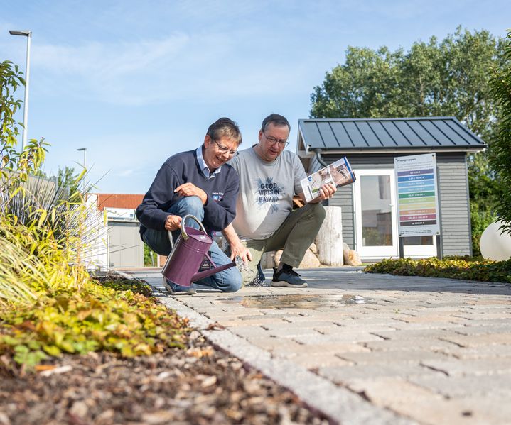 Zwei Menschen prüfen die Versickerung von Wasser auf einer Pflasterfläche im Ideengarten von bauXpert Dittmer