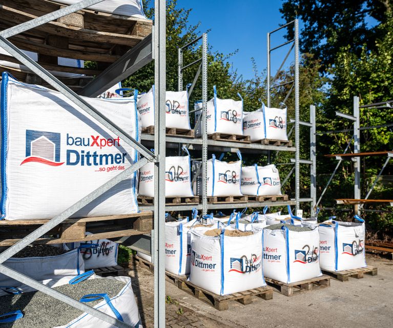 Mehrere Big Bags mit Sand, Kies und Splitt auf dem Lagerplatz von bauXpert Dittmer in Lütjenburg, gestapelt auf Paletten und Regalen.